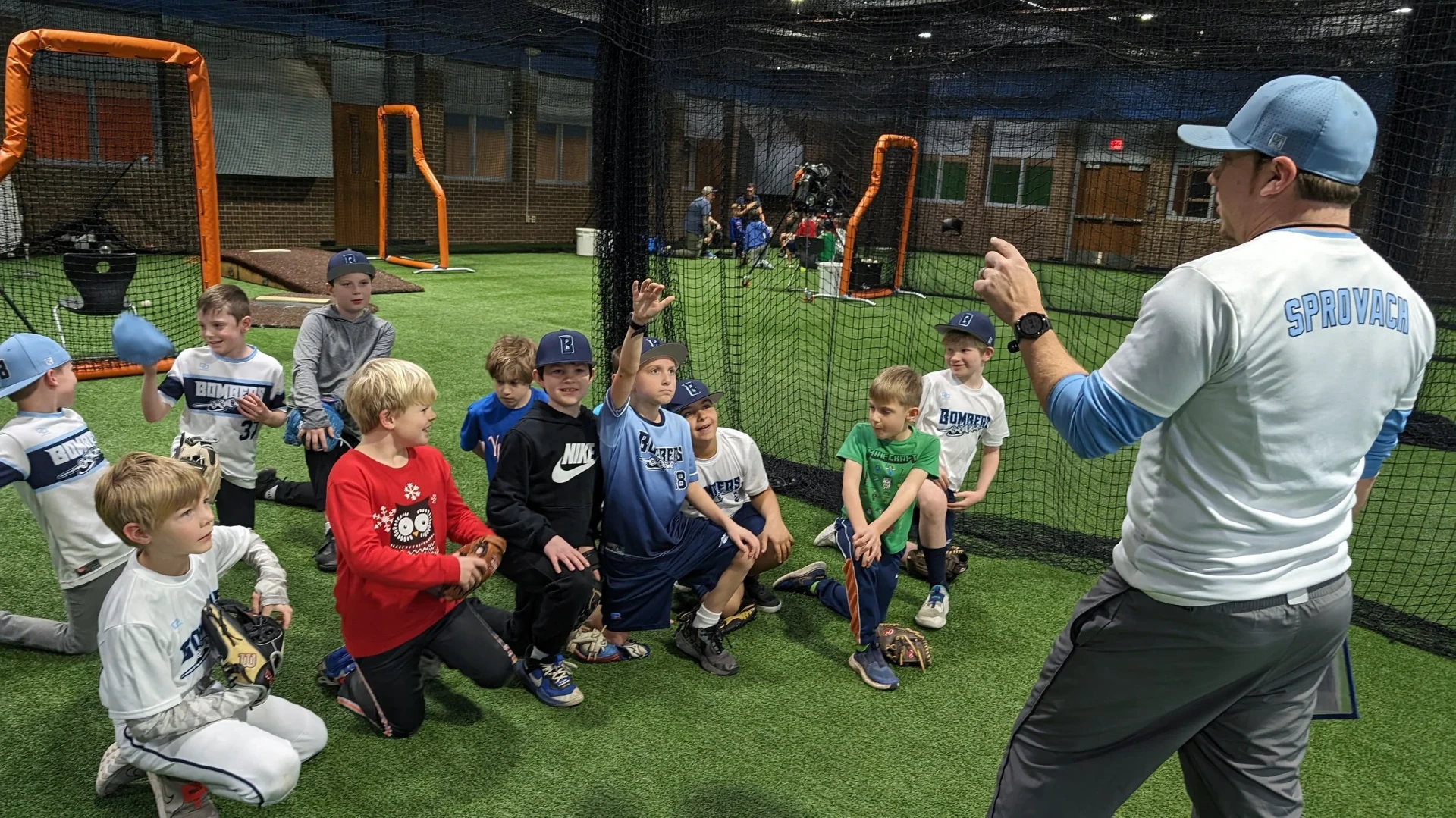 Coach demonstrating throwing mechanics to a group of Bombers players at indoor practice